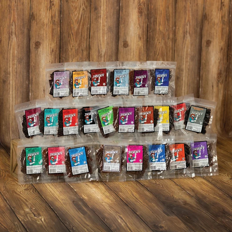 A set of packaged chocolate-covered snacks or bars arranged in three rows on a wooden surface against a wooden plank background. Each package has a different bright color label, and the chocolate pieces are visible through clear plastic bags.